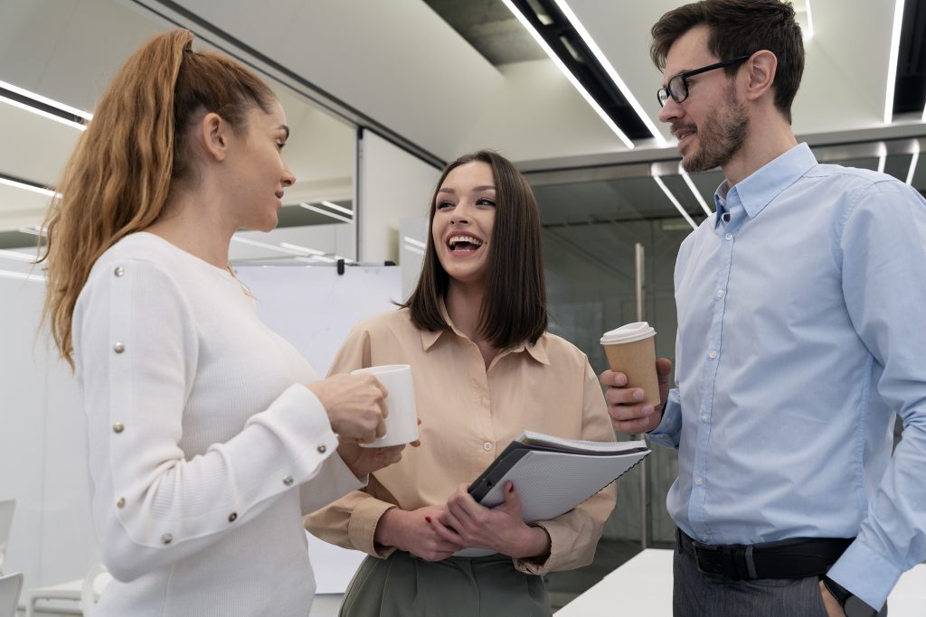 Three coworkers chatting and holding coffee in a modern office.